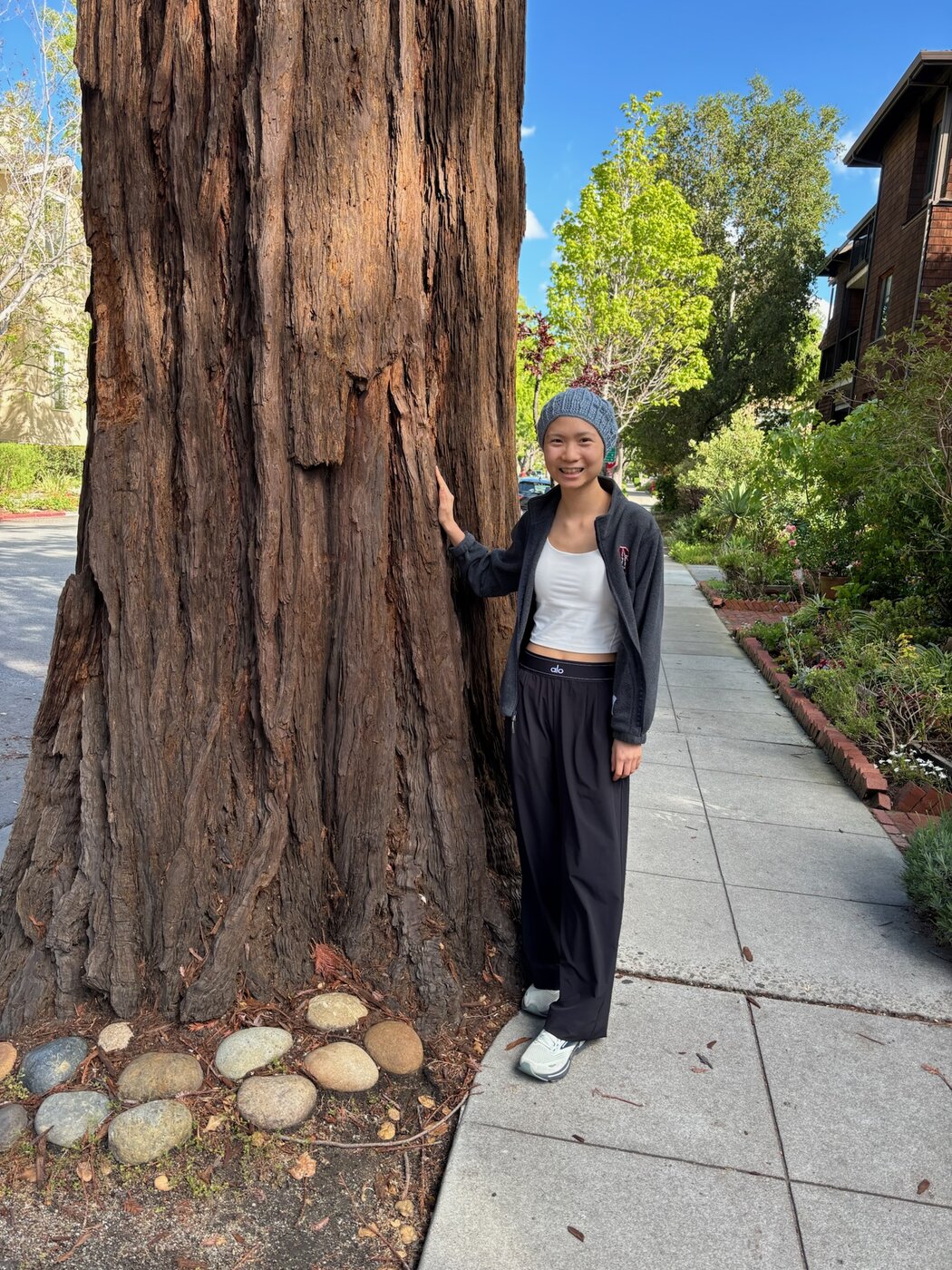 Karis at home in Palo Alto, leaning on a redwood tree — peaceful, present